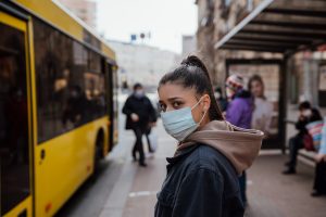 Young woman wearing surgical mask outdoor at bus stop in the street